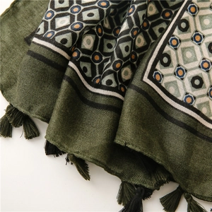 Detail of dark green herringbone scarf featuring geometric prints and black fringe trim