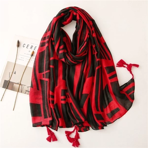 Red and black geometric scarf with fringe tassels laid flat on a white background