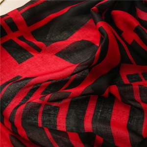 Close-up of red and black geometric scarf fabric showing soft weave texture and fringe