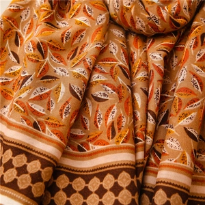 Détail d'une écharpe douce aspect lin avec motifs de feuilles orange et texture tissée