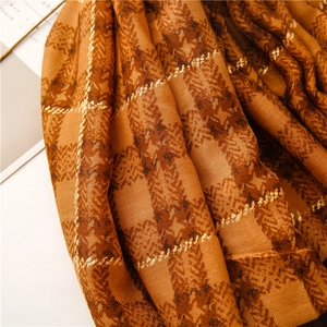 Detailed texture of orange-brown plaid scarf with subtle gold threads and soft fringe
