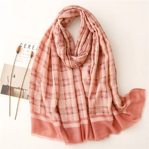 Pink and brick red plaid scarf with gold foil threads and fringed edges on a flat surface