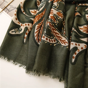 Makro-Detail von dunkelgrünem Fischgrät-Schal mit goldenen Paisley-Blattmustern