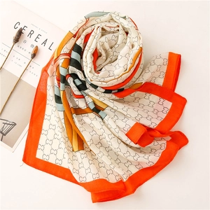 Detailed view of the luxury monogram print and vibrant orange border on the silk shawl