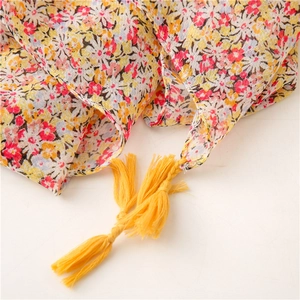 Detail of floral print scarf with bright yellow fringe tassels on breathable fabric