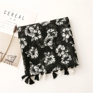 Soft black scarf with white floral print and tassel edges on minimalist background
