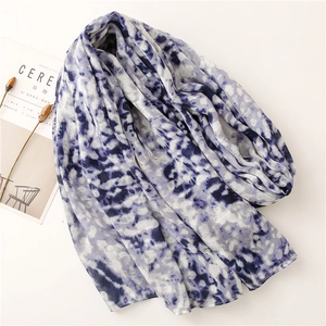 Flat lay of soft blue and white tie-dye scarf with aesthetic magazine and dried flowers