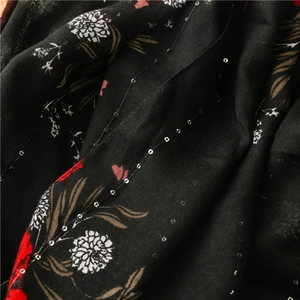 Détail d'une écharpe florale avec paillettes argentées sur tissu en lin et coton noir