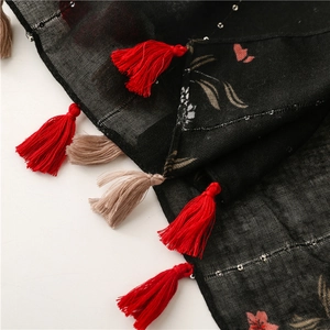 Gros plan d'une écharpe fleurie noire avec fleurs roses, paillettes argentées et franges