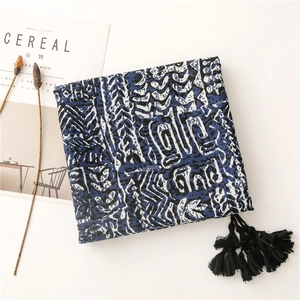 Détail d'un châle bleu à motifs géométriques et pompons noirs sur fond blanc minimaliste