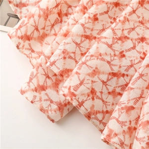 Detail eines weichen Baumwoll-Leinen-Schals mit orangefarbener Batik-Struktur und Falten
