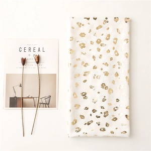 Detail of white cotton scarf with gold leopard print beside minimalist magazines