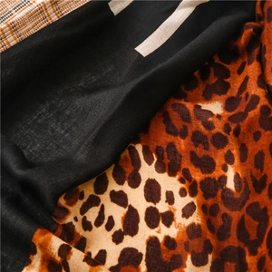 Detail of soft scarf featuring leopard print, solid black, and orange check patterns
