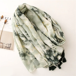 Detail of sage green scarf with ink art pattern and black tassels on white backdrop