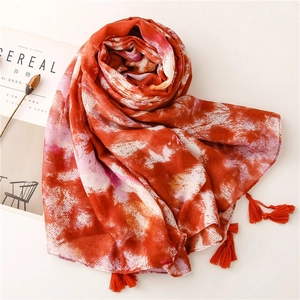 Detailed view of orange and white tie-dye scarf with fringe tassels on beige background