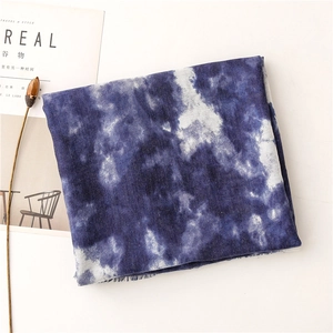Dettaglio di sciarpa in cotone tie-dye blu e bianco con nappe su sfondo minimalista