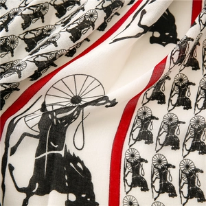 Detailed close-up of silk-textured scarf with horse carriage patterns and red borders
