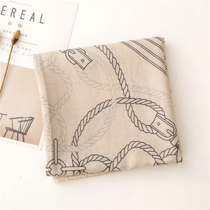 Dettaglio di sciarpa beige in cotone e lino con stampa a corda accanto a rivista