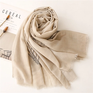Dettaglio di sciarpa beige con linee botaniche nere e bordi con frange delicate