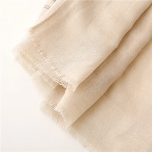 Macro dettaglio della sciarpa in cotone-lino beige con trama fine e bordi con frange