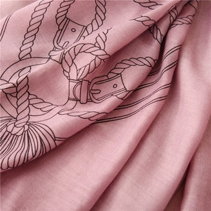 Dettaglio di sciarpa in seta rosa con motivi equestri e nappe in una texture drappeggiata