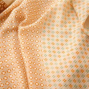 Dettaglio di sciarpa beige con motivi a trifoglio arancio e verdi su tessuto in chiffon