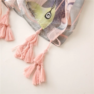 Détail d'une écharpe rose et grise avec motifs d'oiseaux et finitions à franges