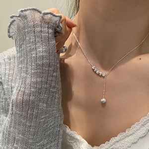 Détail d'un collier en Y argenté avec perles métalliques et pendentif rond sur le cou