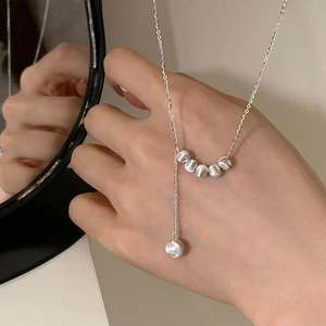 Détail macro du collier argenté en S avec perles en métal brossé sur une chaîne fine