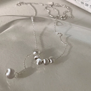 Détail d'un collier en argent avec six perles mates sur un plateau en verre