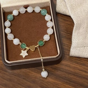 Détail d'un bracelet en perles avec pierres vertes et breloque cœur doré en boîte