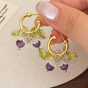 Detailed close-up of handmade gold hoop earrings with purple beads and green stone drops