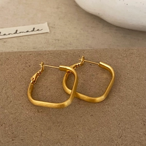 Détail de boucles d'oreilles carrées en or mat avec une texture métallique brossée