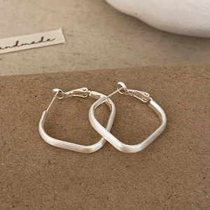 Détail de boucles d'oreilles carrées en métal argenté avec finition brossée mate