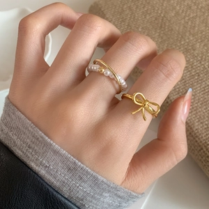 Elegant gold bow ring with pearl layer detail shown on model hand in a soft aesthetic