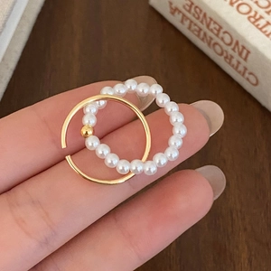 Detail of elegant gold beaded ring and white pearl elastic ring set on a warm wood background
