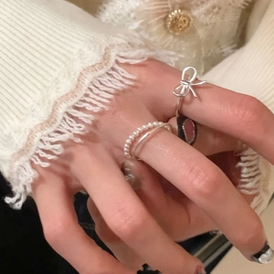 Close-up of pearl bow and red heart rings styled on a white lace sleeve background