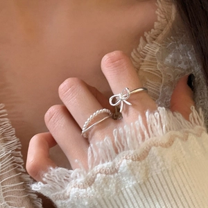 Detail of silver bow ring and double pearl chain ring set worn on a finger