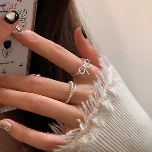 Macro view of silver bow ribbon ring and delicate pearl band worn for layering
