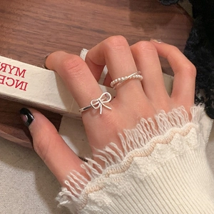 Detail of silver bow ring and pearl crossover ring set worn with lace sleeve details