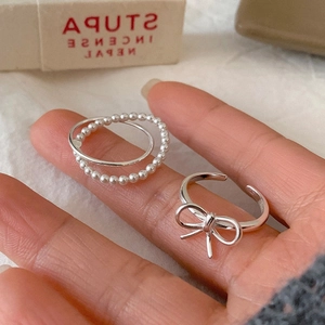 Detailed close-up of silver bow ring and layered beaded band worn on a hand