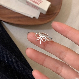 Detailed view of silver bow-shaped open ring worn on finger in a cozy minimalist setting