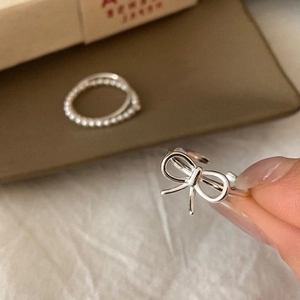 Detailed close-up of a silver bow ring with adjustable thin band on a textured background