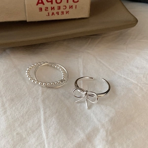 Silver bow and layered bead ring set displayed on a rustic ceramic tray with fabric