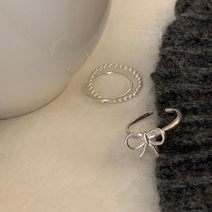 Close-up of a silver bow ring and a minimalist beaded band set on white ceramic