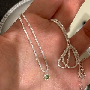 Close-up of elegant silver chain necklace featuring a sparkling round green zircon pendant