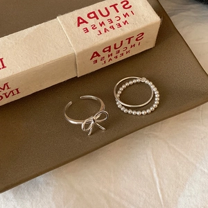 Detail of silver bow ring and pearl beaded ring set on a brown jewelry display tray