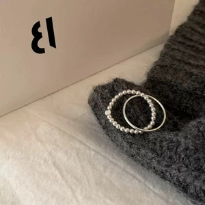 Detail view of a silver bead ring and minimalist thin band set on a grey knit fabric
