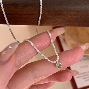 Detail of silver link necklace featuring a sparkling green zircon pendant on a woman's finger