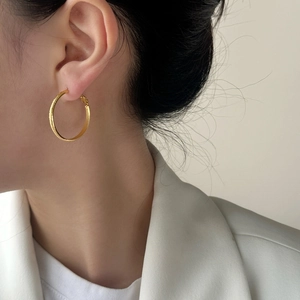 Textured gold hoop earrings with matte brushed finish worn by a model in white blazer